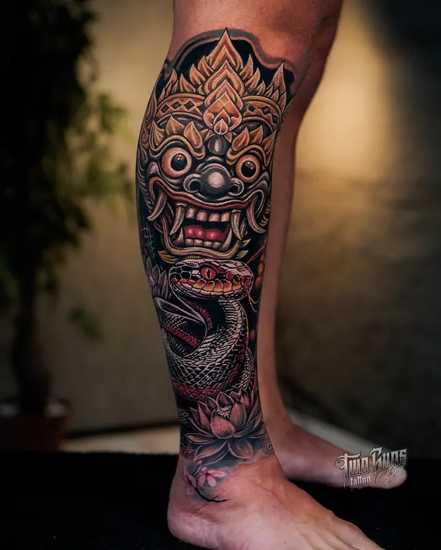 Colour Balinese Barong mask calf tattoo with a gold crown, coiled snake and lotus flowers