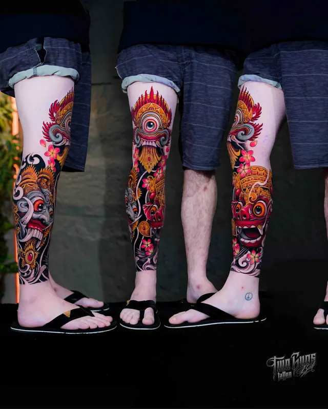 Colour Balinese leg sleeve tattoo of Barong and Rangda masks in red and gold with frangipani