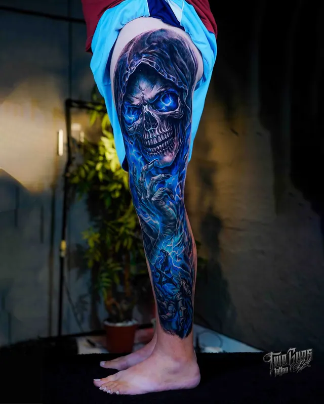 Colour realism leg sleeve tattoo of a hooded skull lit in blue