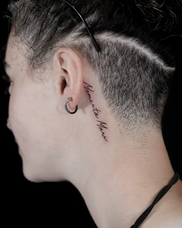 Small fine line script tattoo behind the ear on a woman with a shaved undercut