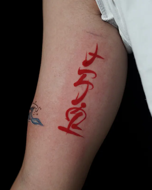 Japanese brush script tattoo in red ink on the upper arm