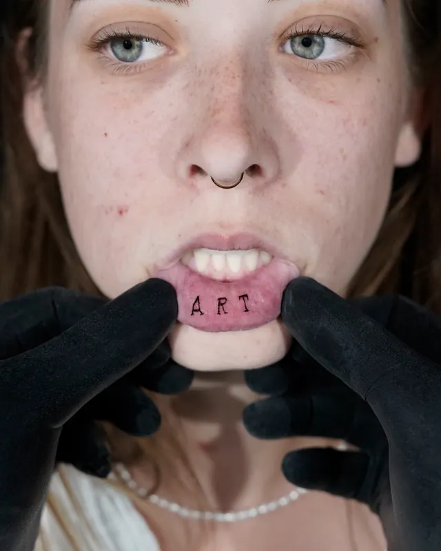 Inner lip tattoo reading Art in small block letters