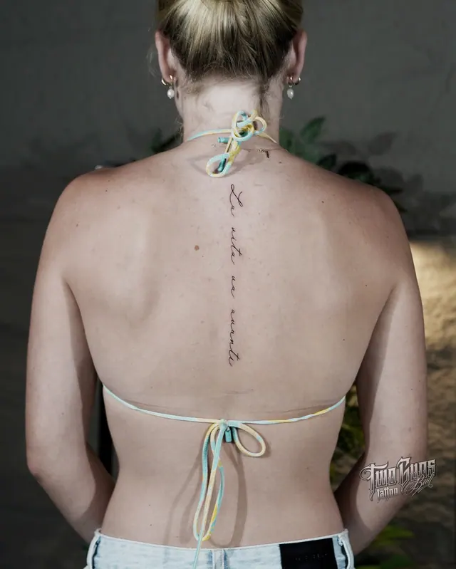 Small fine line script tattoo running down a woman's upper spine