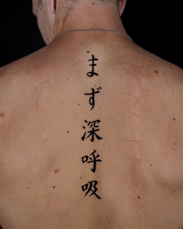 Japanese spine tattoo in black brush script down a man's upper back