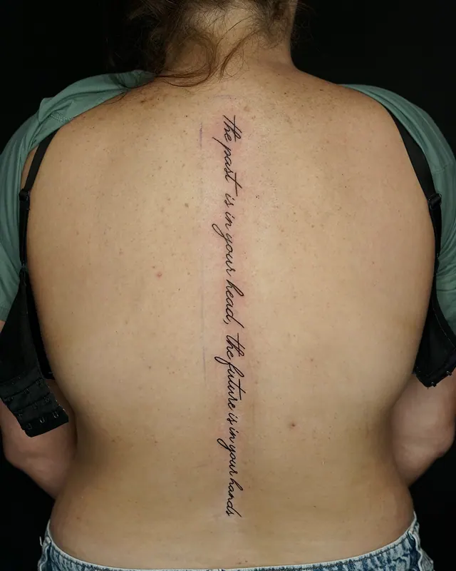 Fine line script tattoo running the full length of a woman's spine