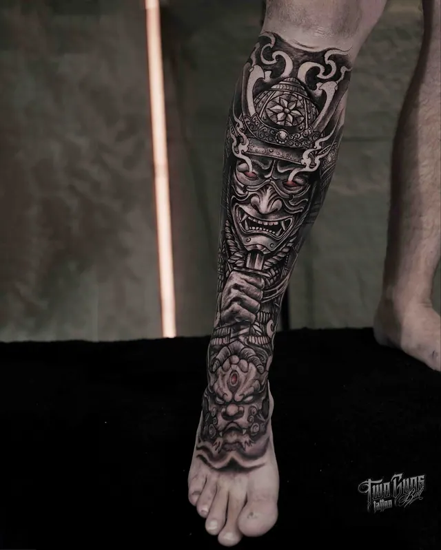 Black and grey Japanese lower leg tattoo of a hannya mask with waves