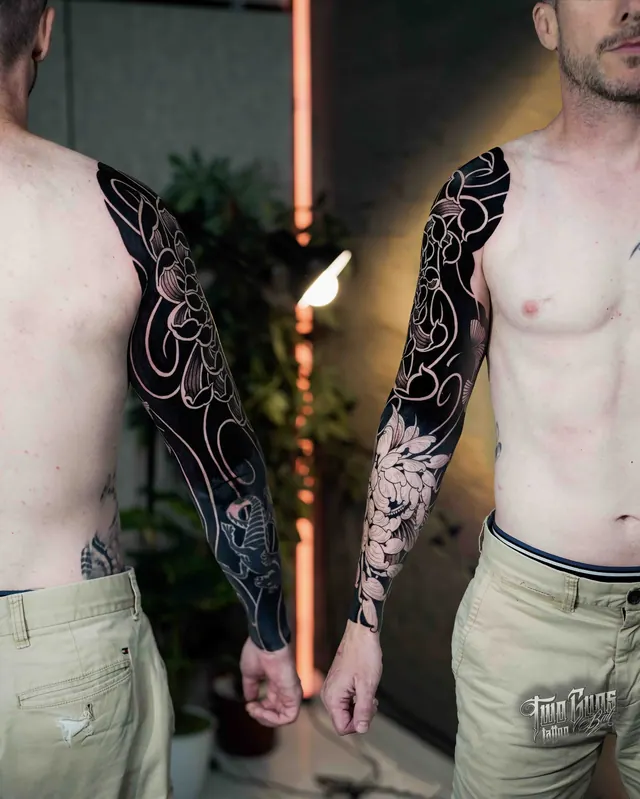 Blackwork full sleeve tattoos with negative space florals, shown on two clients