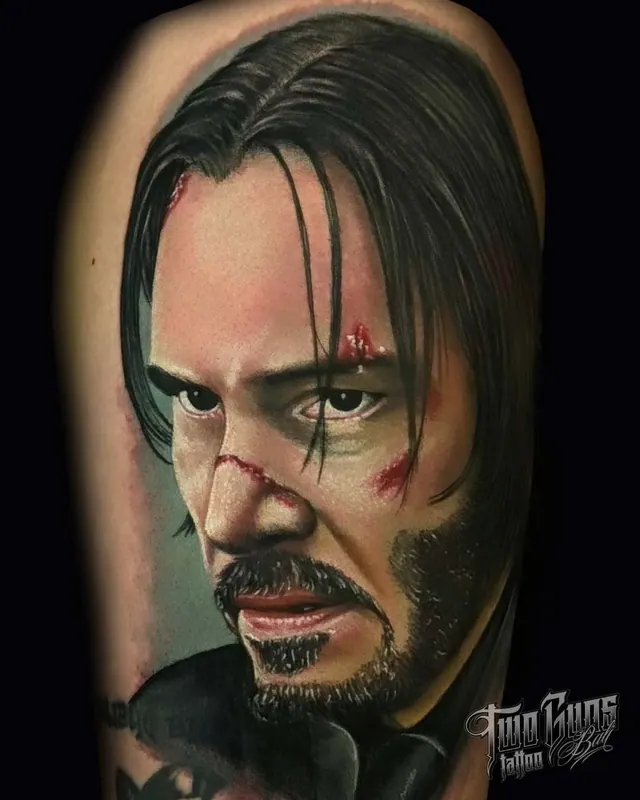 Colour realism upper arm portrait tattoo of John Wick