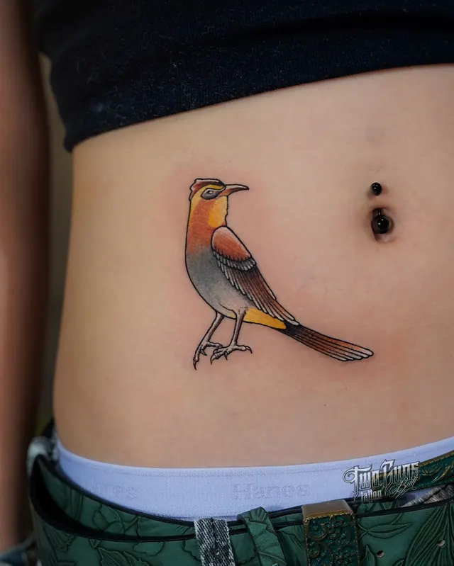 Small colour tattoo of a robin perched, on the hip