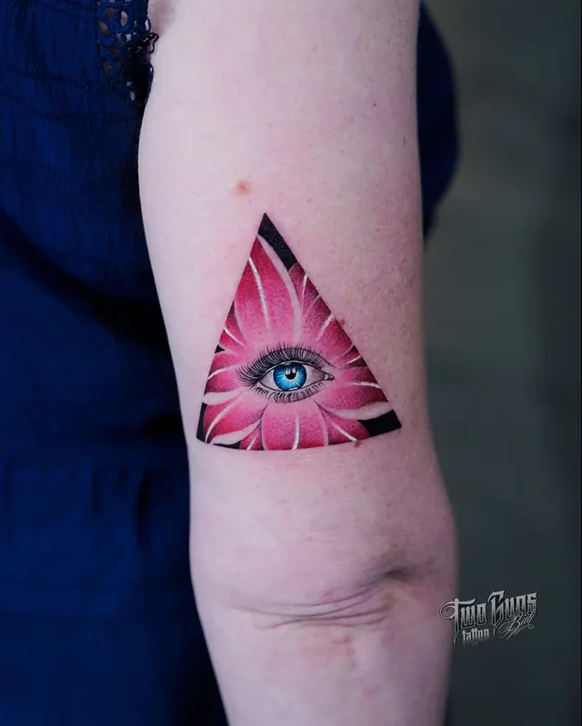 Upper arm tattoo of an eye inside a triangle in pink and black