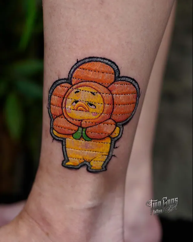 Small colour cartoon chick in a flower costume, tattooed on the ankle