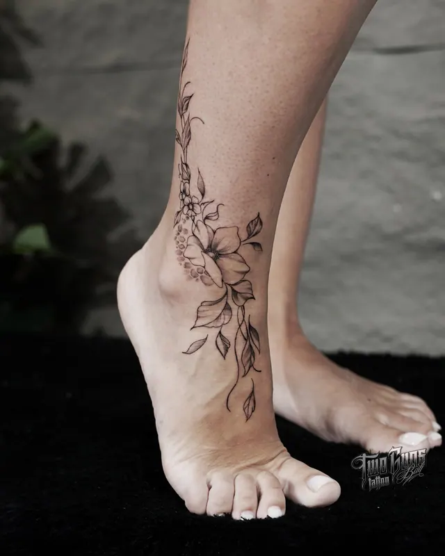 Fine line floral vine tattoo wrapping a woman's ankle and foot