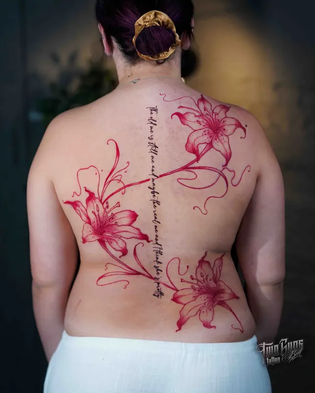Red and pink lily back tattoo with a trailing vine and fine line script down the spine