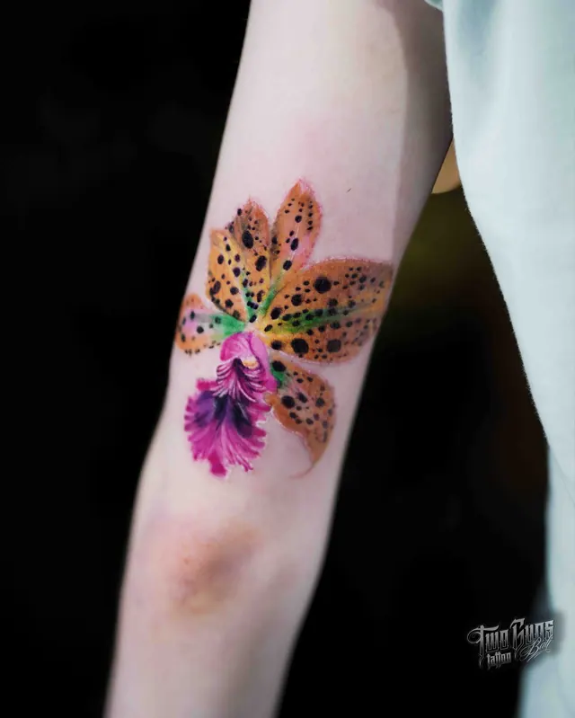 Colour watercolour-style orchid tattoo on a woman's forearm in pink and yellow