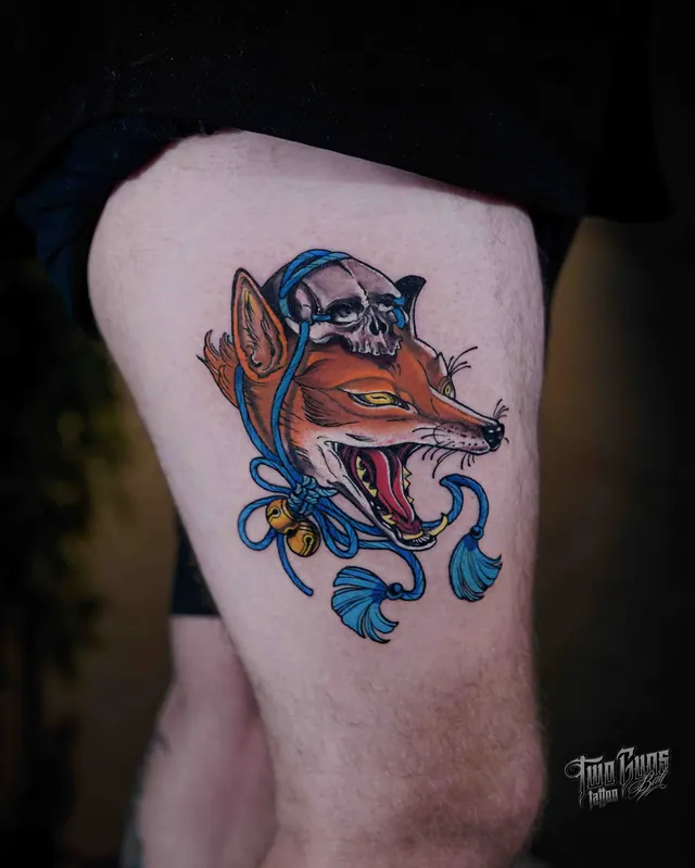 Neo-traditional thigh tattoo of a fox head with a blue ribbon and skull
