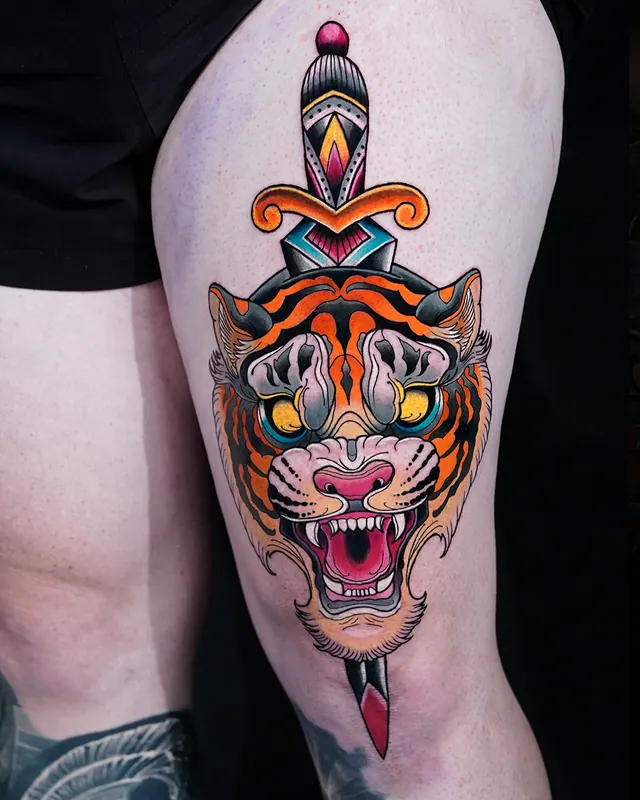 Colour traditional thigh tattoo of a tiger head pierced by a dagger