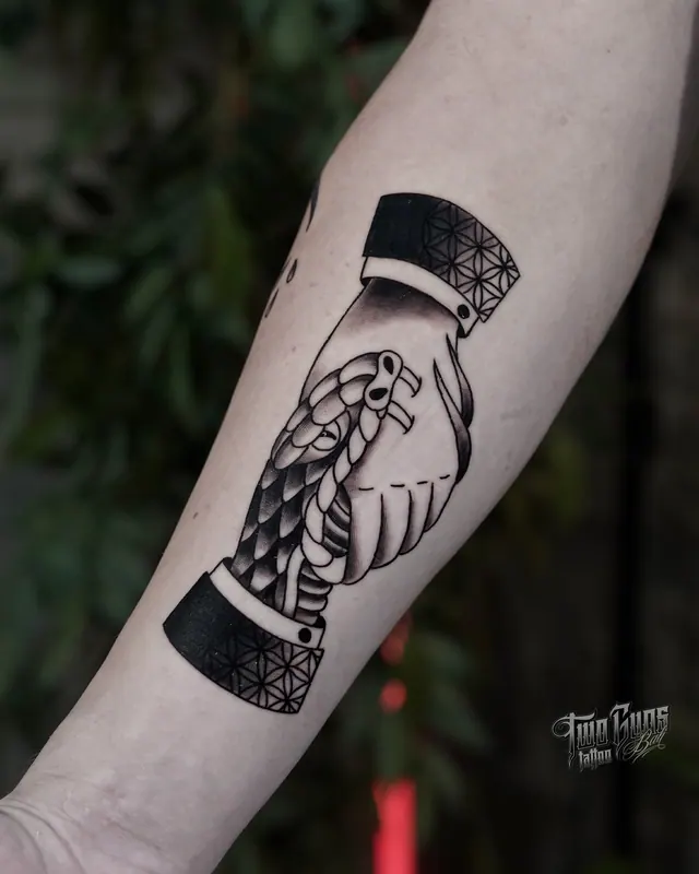 Blackwork forearm tattoo of two hands clasped in a handshake with lace cuffs