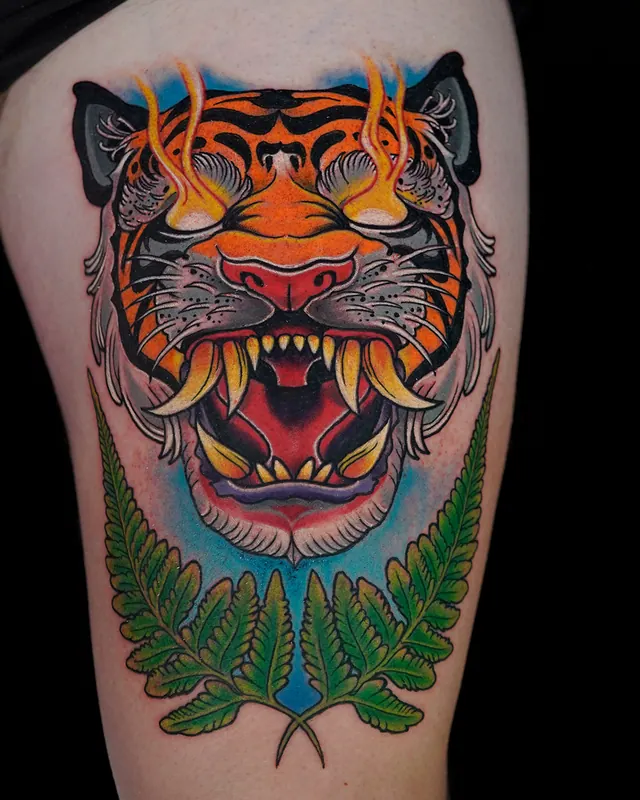 Neo-traditional thigh tattoo of a roaring tiger head with ferns